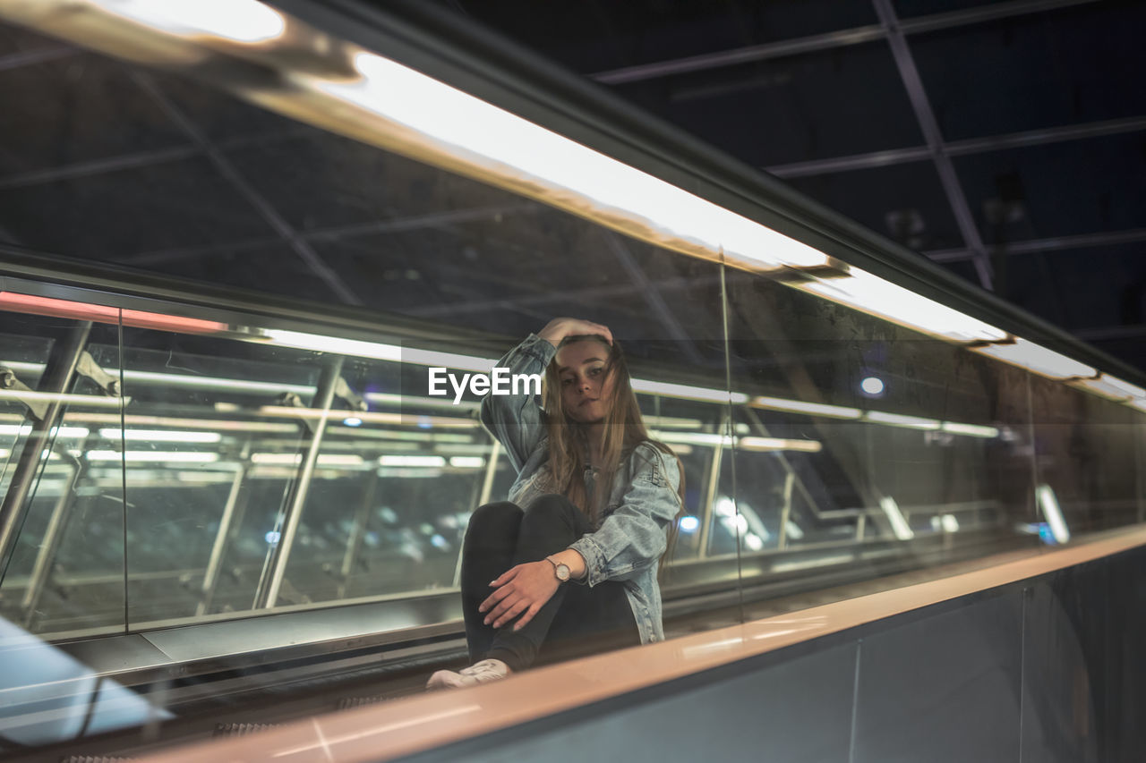 Portrait of woman sitting on escalator in city at night