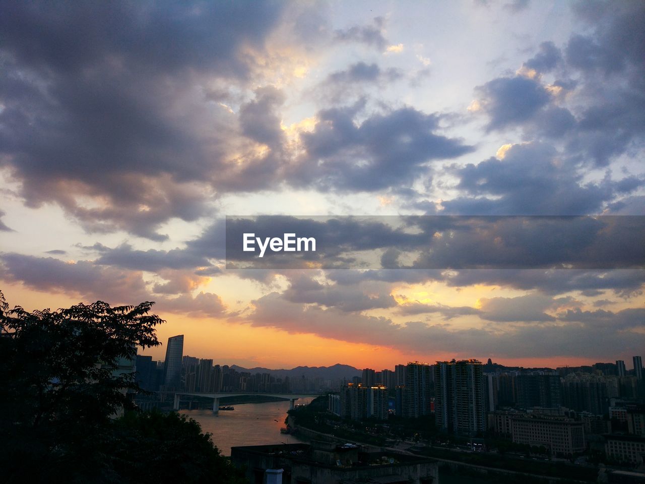 Silhouette of city against cloudy sky during sunset