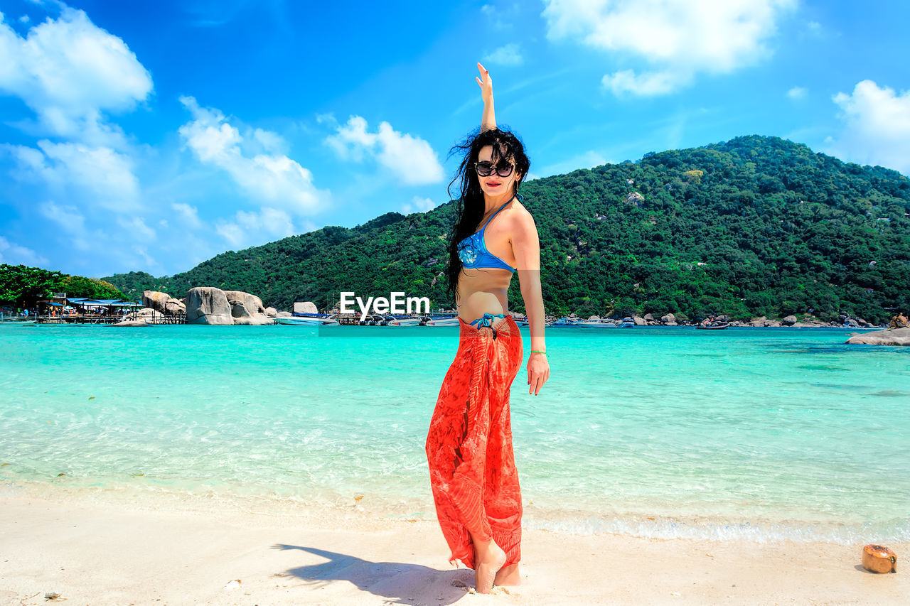 YOUNG WOMAN STANDING ON BEACH AGAINST SKY