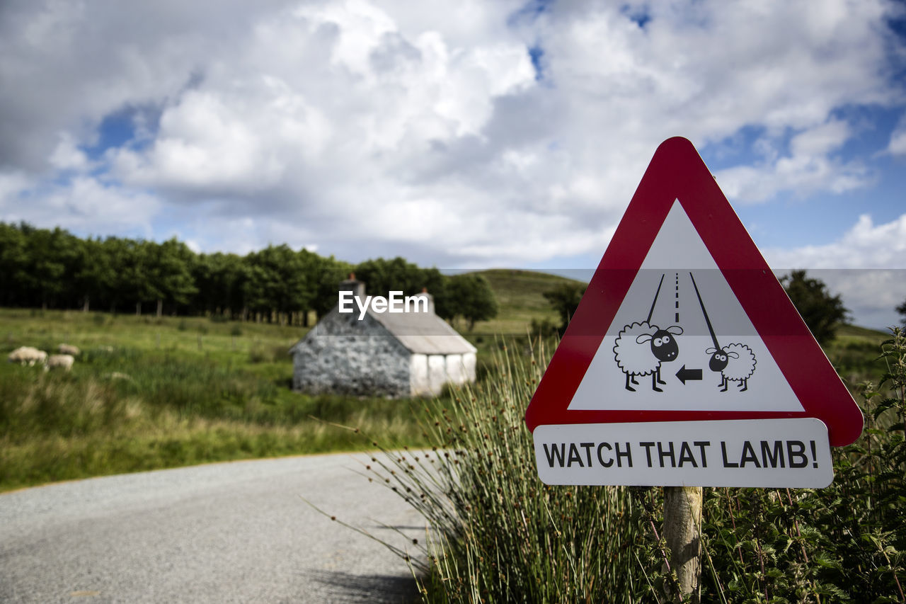 Information sign on roadside by plants against cloudy sky