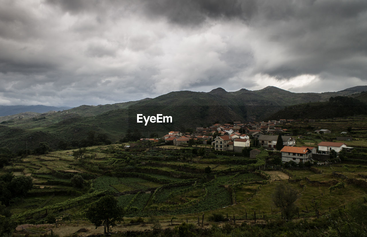 Houses in village on green landscape against cloudy sky