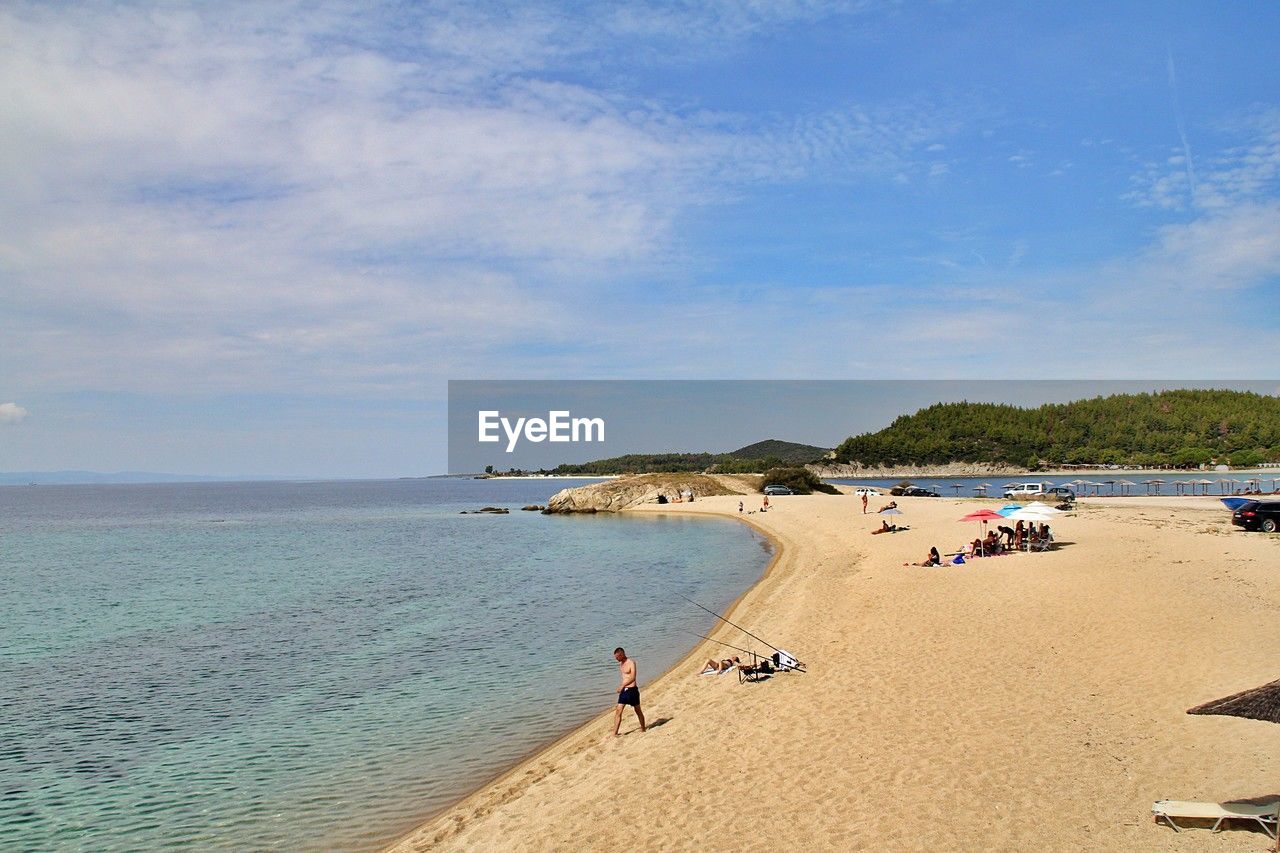 land, beach, water, sea, sky, body of water, sand, nature, holiday, vacation, shore, trip, coast, ocean, scenics - nature, beauty in nature, travel, travel destinations, cloud, coastline, summer, tourism, day, tranquility, bay, leisure activity, blue, water's edge, group of people, sunlight, outdoors, tranquil scene, relaxation, idyllic, tourist, horizon, horizon over water, environment, sunny, landscape, transportation, adult, large group of people, lifestyles, seascape, tree, men, island, non-urban scene, sports, tropical climate