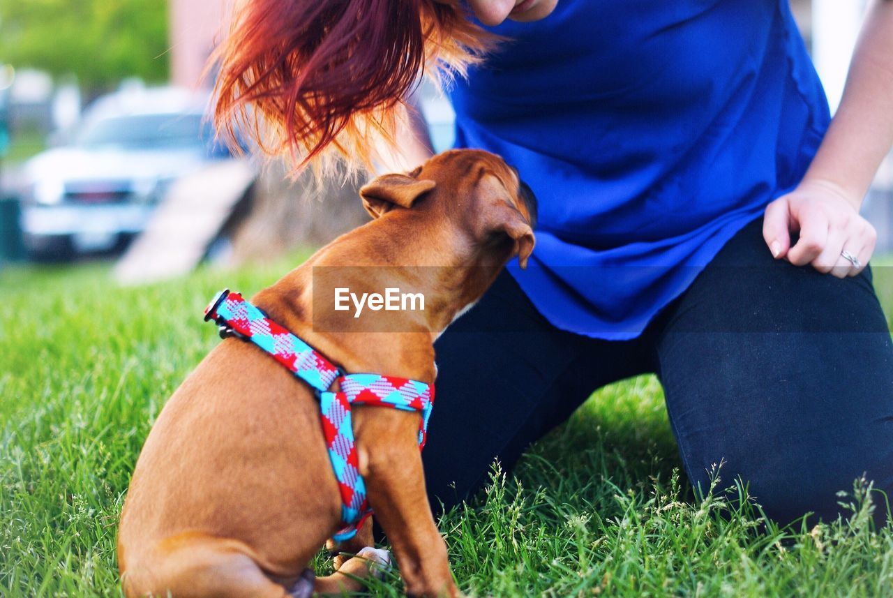 Close-up of woman playing with puppy on grassy field