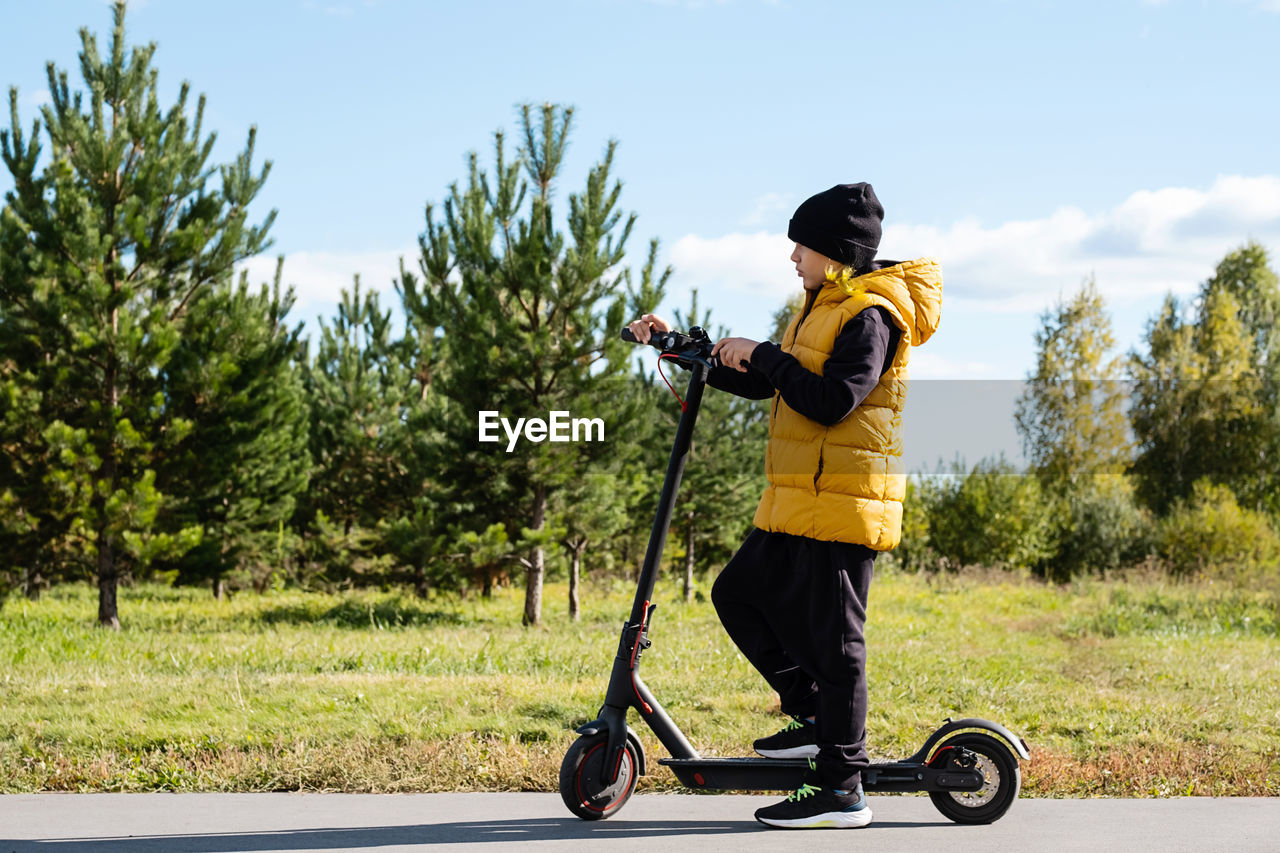 Boy rides an electric scooter in autumn park. schoolboy using e-scooter at sunny day.