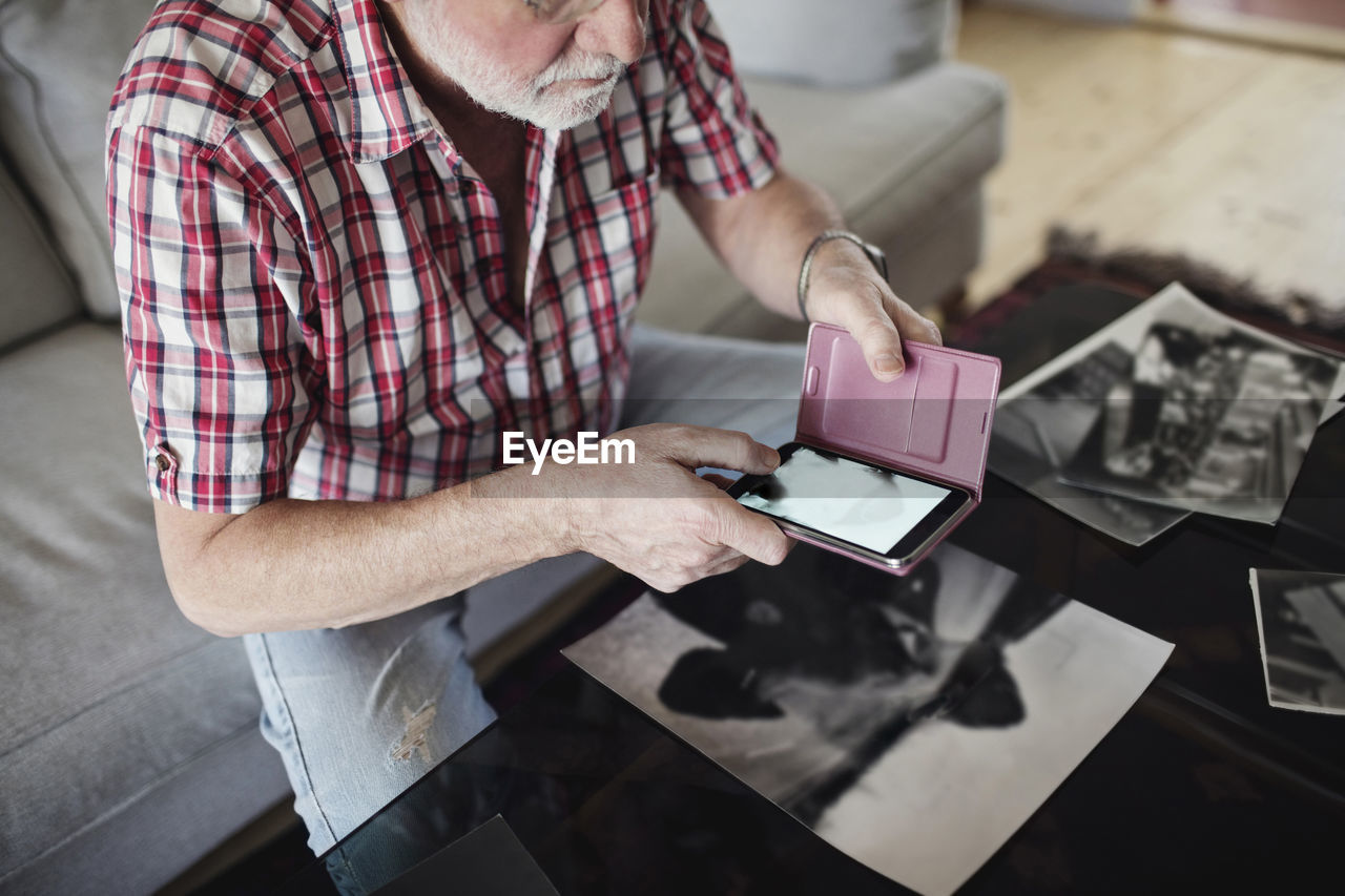 Midsection of senior man photographing old photograph through smart phone at home