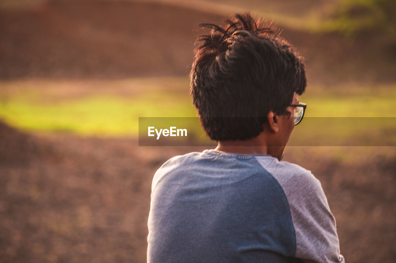 Rear view of young man sitting on field