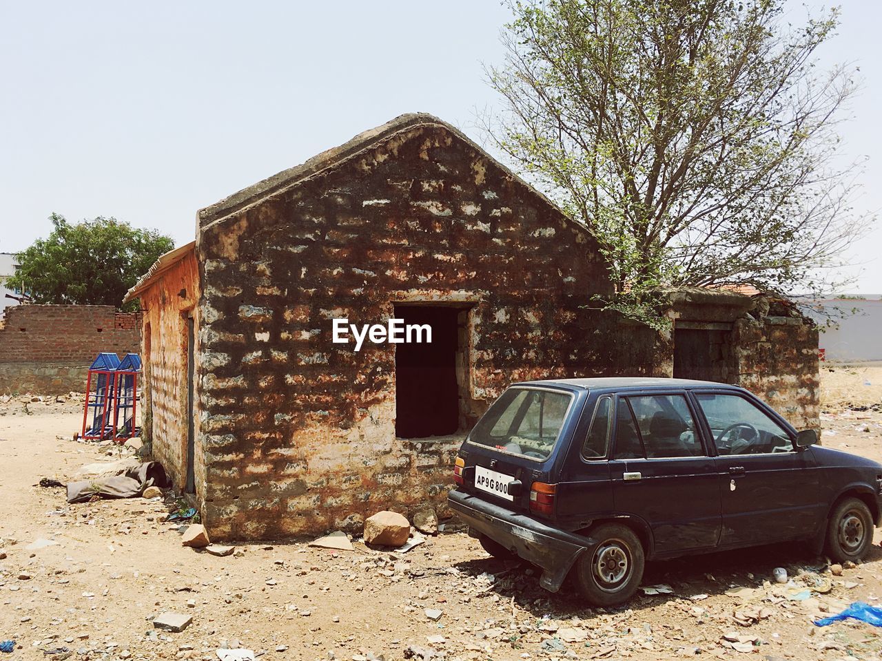 ABANDONED CAR ON FIELD AGAINST BUILDINGS