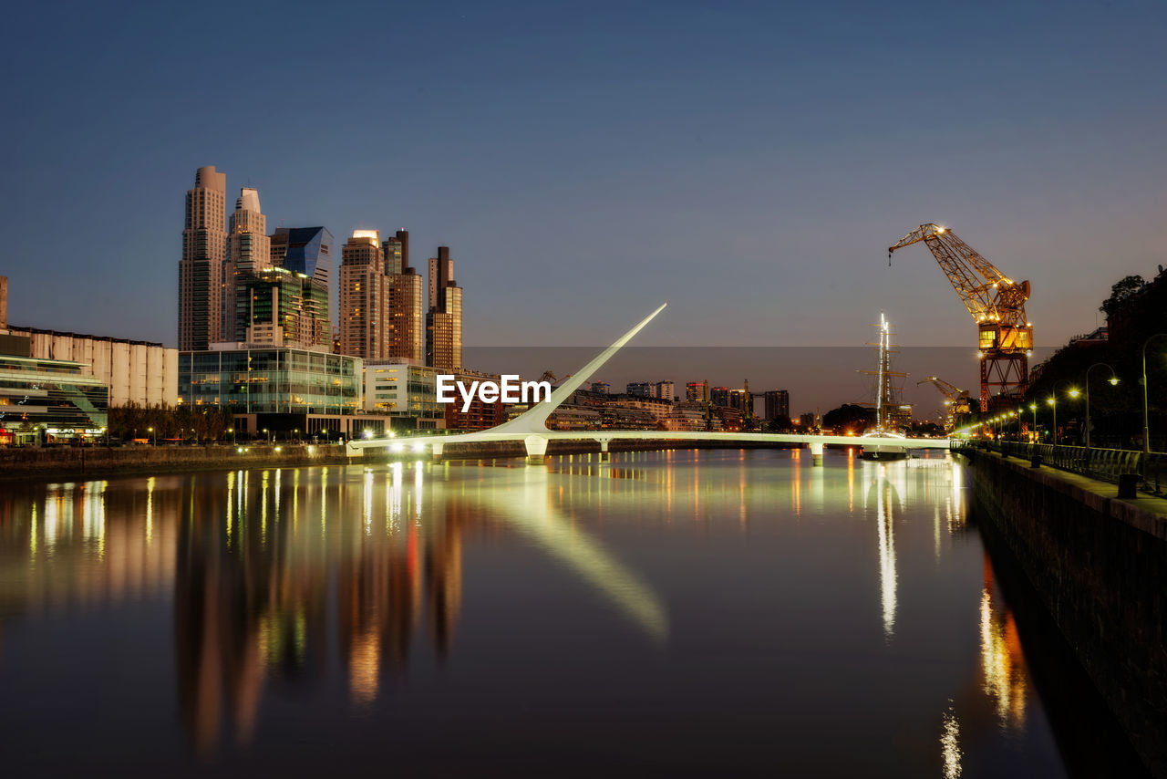 ILLUMINATED MODERN BUILDINGS BY RIVER AGAINST SKY