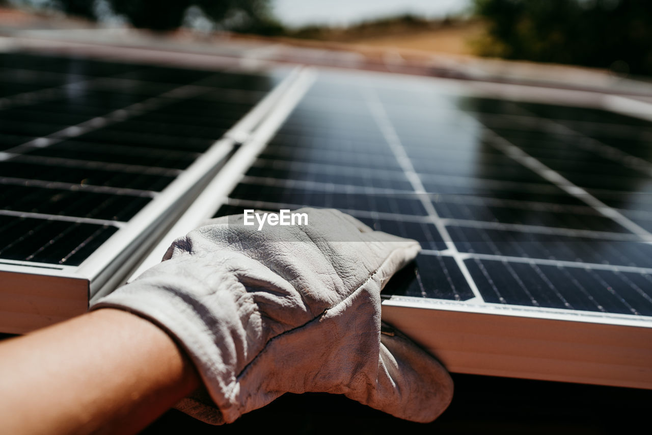 Hand of mature technician man touching solar panels on house roof for self consumption energy