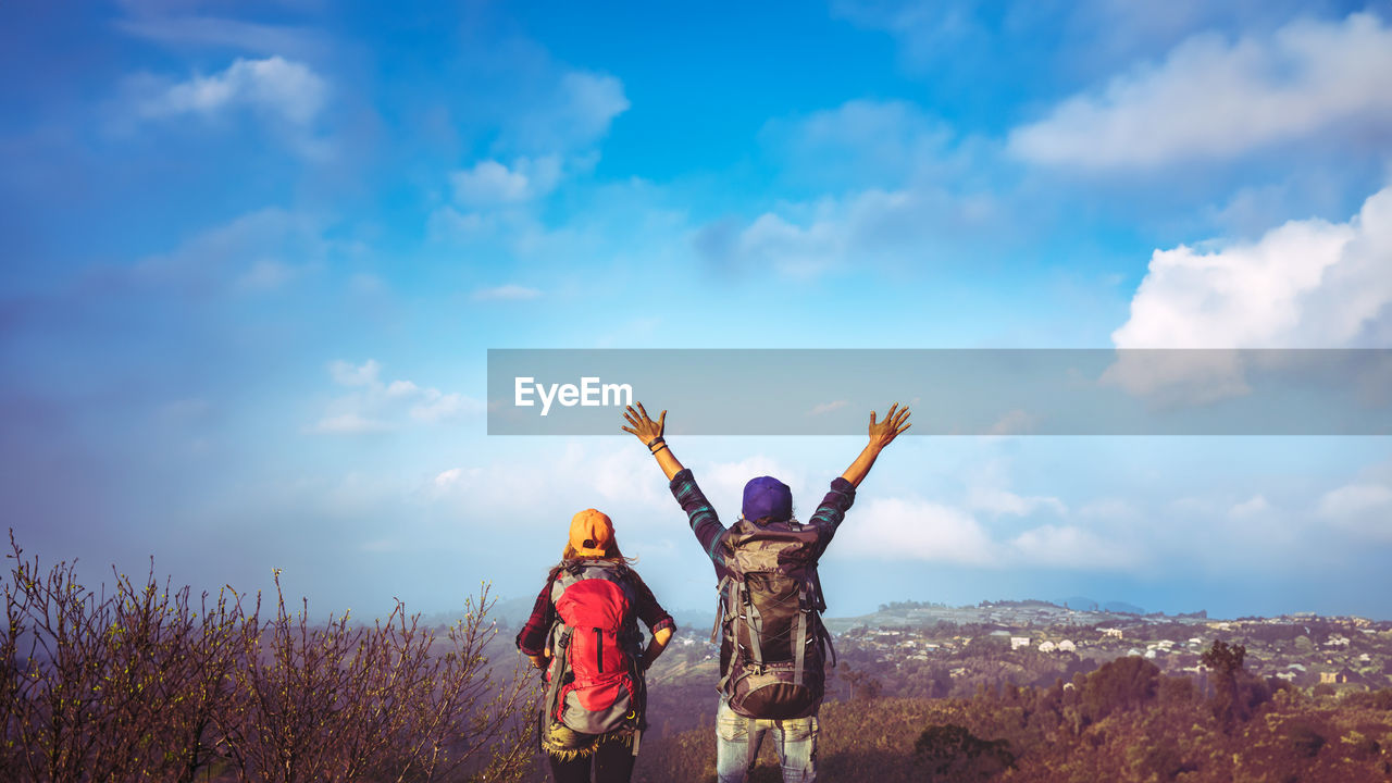 sky, cloud, mountain, nature, arm, adult, landscape, limb, women, human limb, two people, togetherness, hiking, leisure activity, arms raised, environment, adventure, standing, child, female, full length, happiness, scenics - nature, beauty in nature, day, men, childhood, outdoors, copy space, land, holiday, travel, blue, tree, emotion, positive emotion, backpack, vacation, clothing, trip, person, enjoyment, activity, friendship, young adult, lifestyles, sunlight, rear view, plant, carefree, travel destinations, casual clothing, bonding, non-urban scene, success, smiling