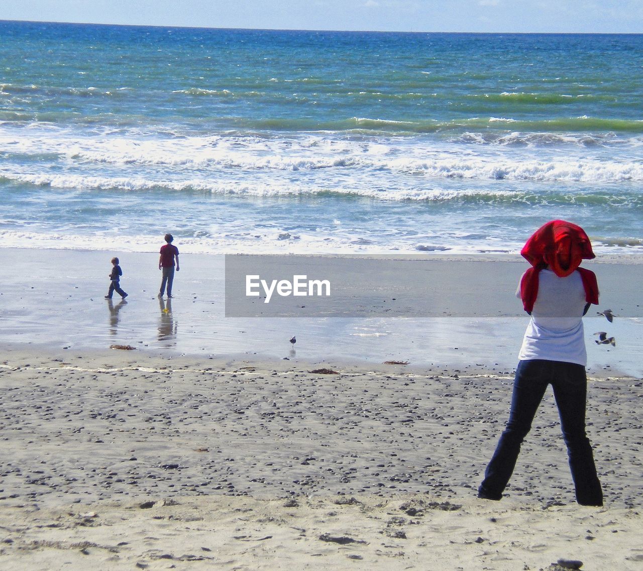 REAR VIEW OF WOMEN STANDING AT BEACH AGAINST SEA