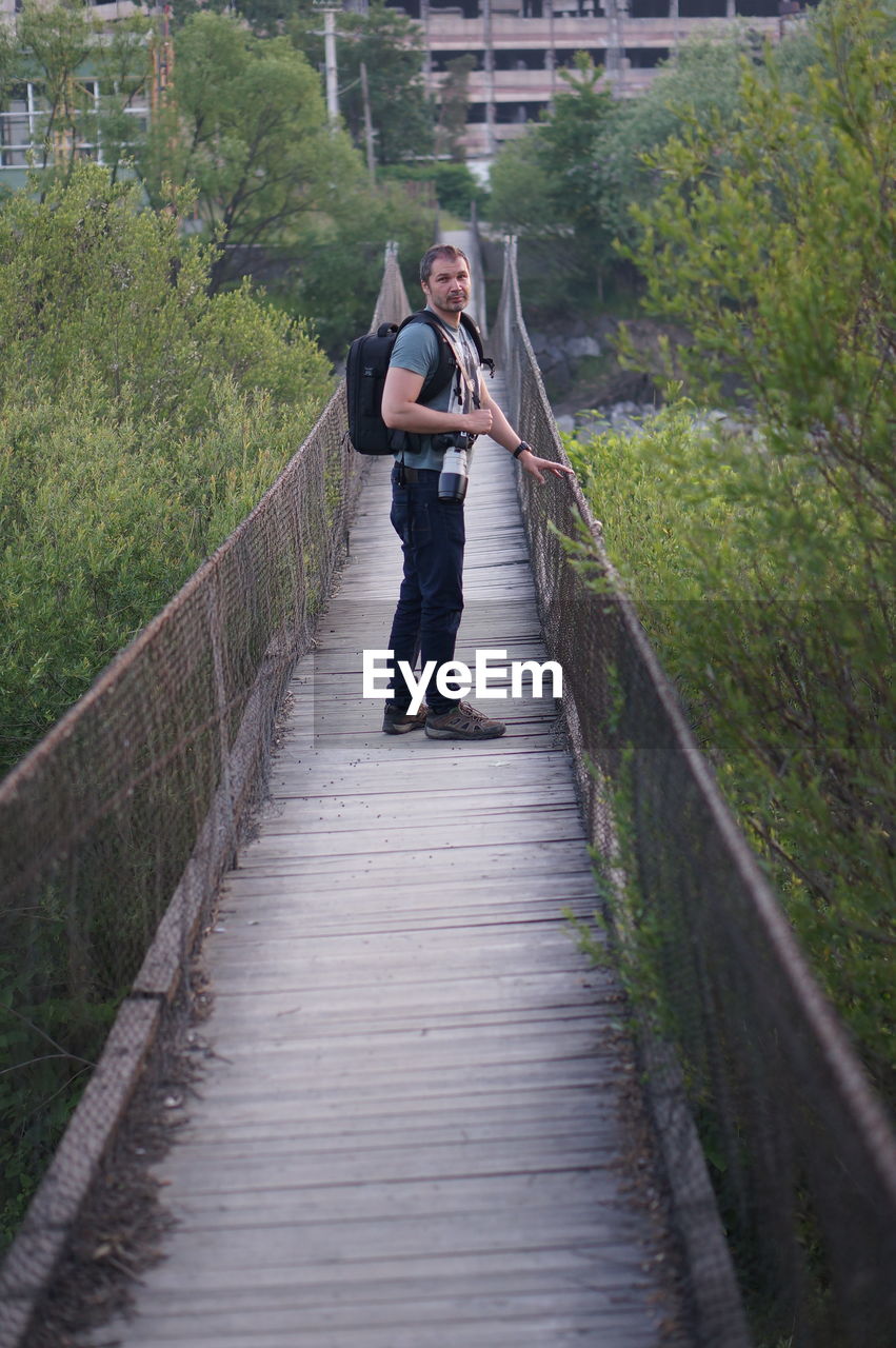 Full length portrait of man standing amidst trees on footbridge