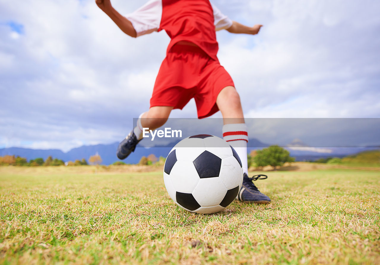 low section of man playing soccer on field against cloudy sky