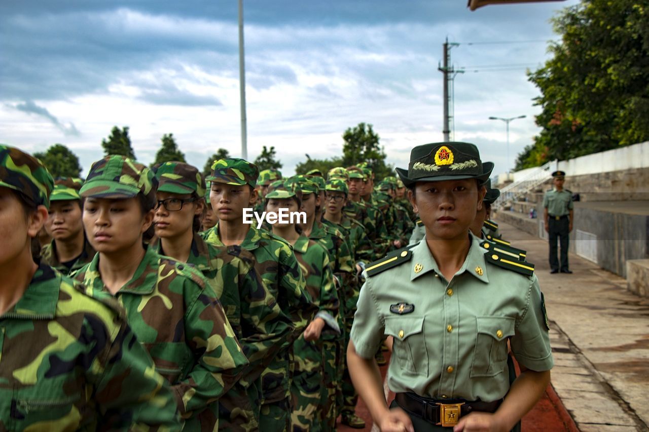 Female army soldiers standing on road against cloudy sky