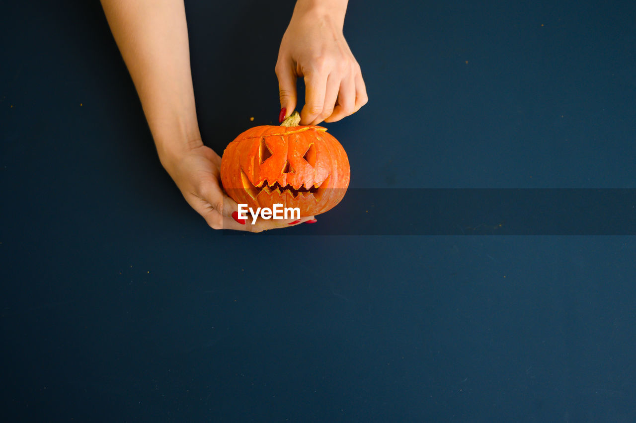 Low angle view of hand holding pumpkin against blue background