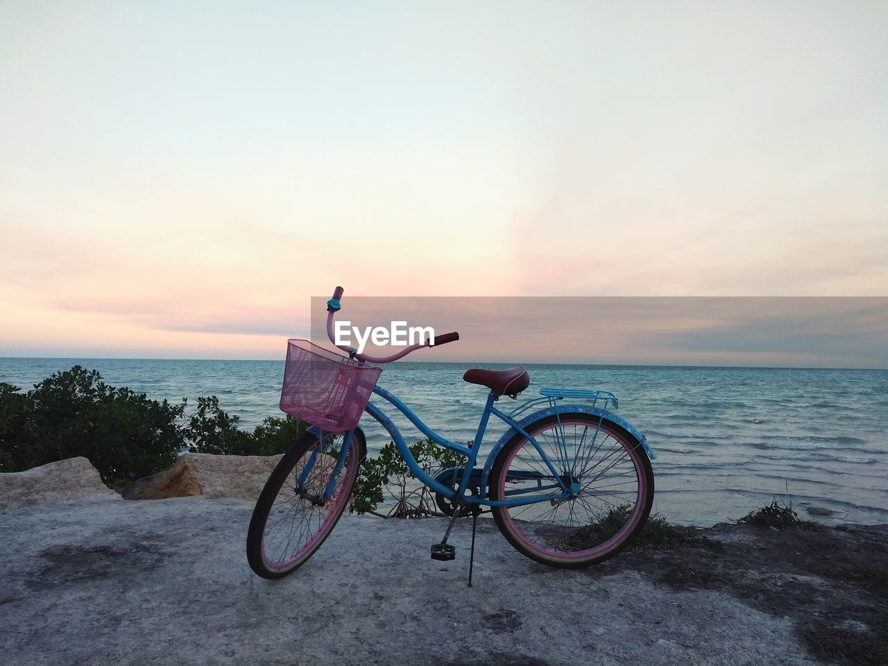 Bicycle on beach against sky during sunset