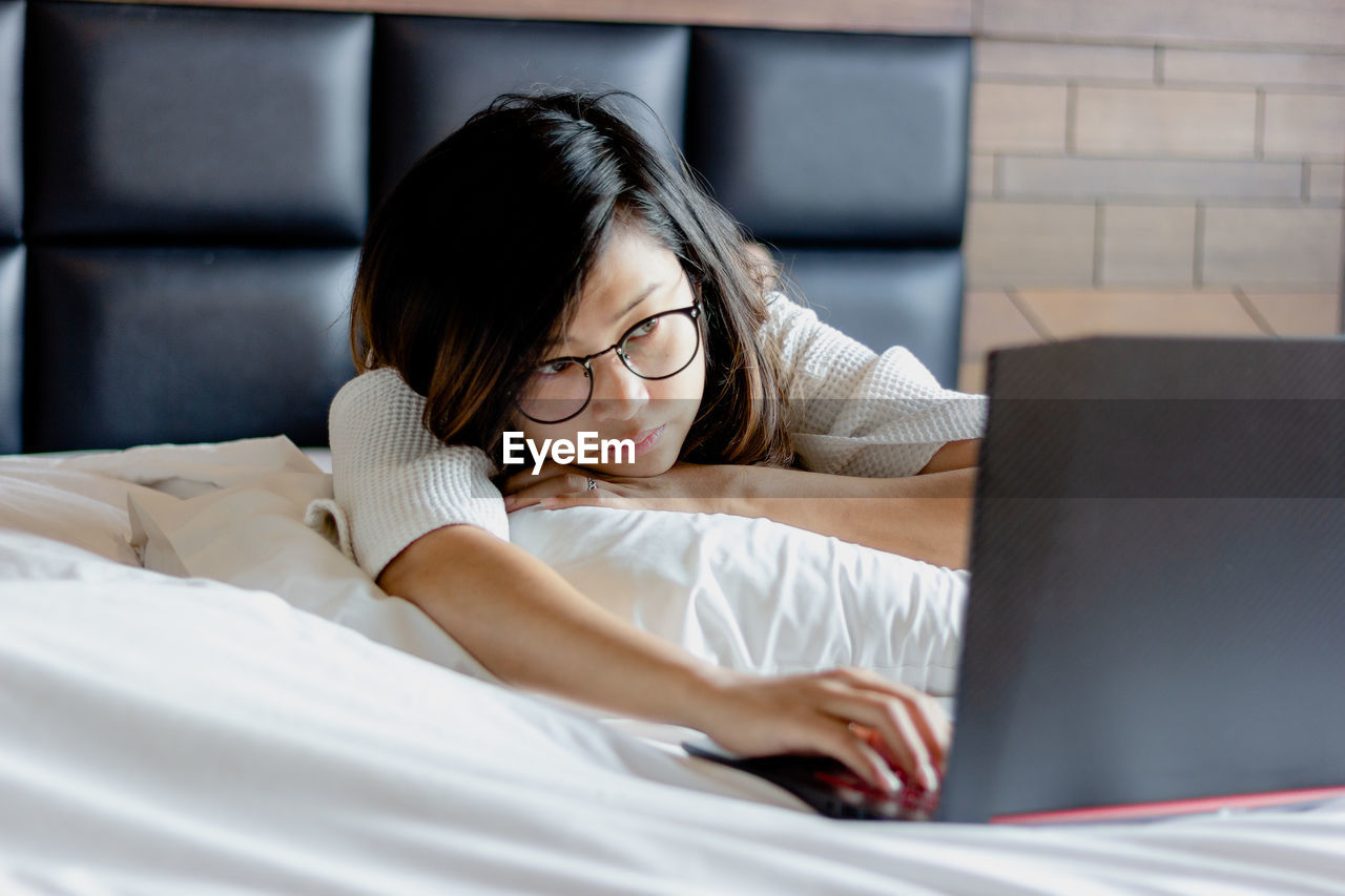Woman using laptop while lying on bed at home