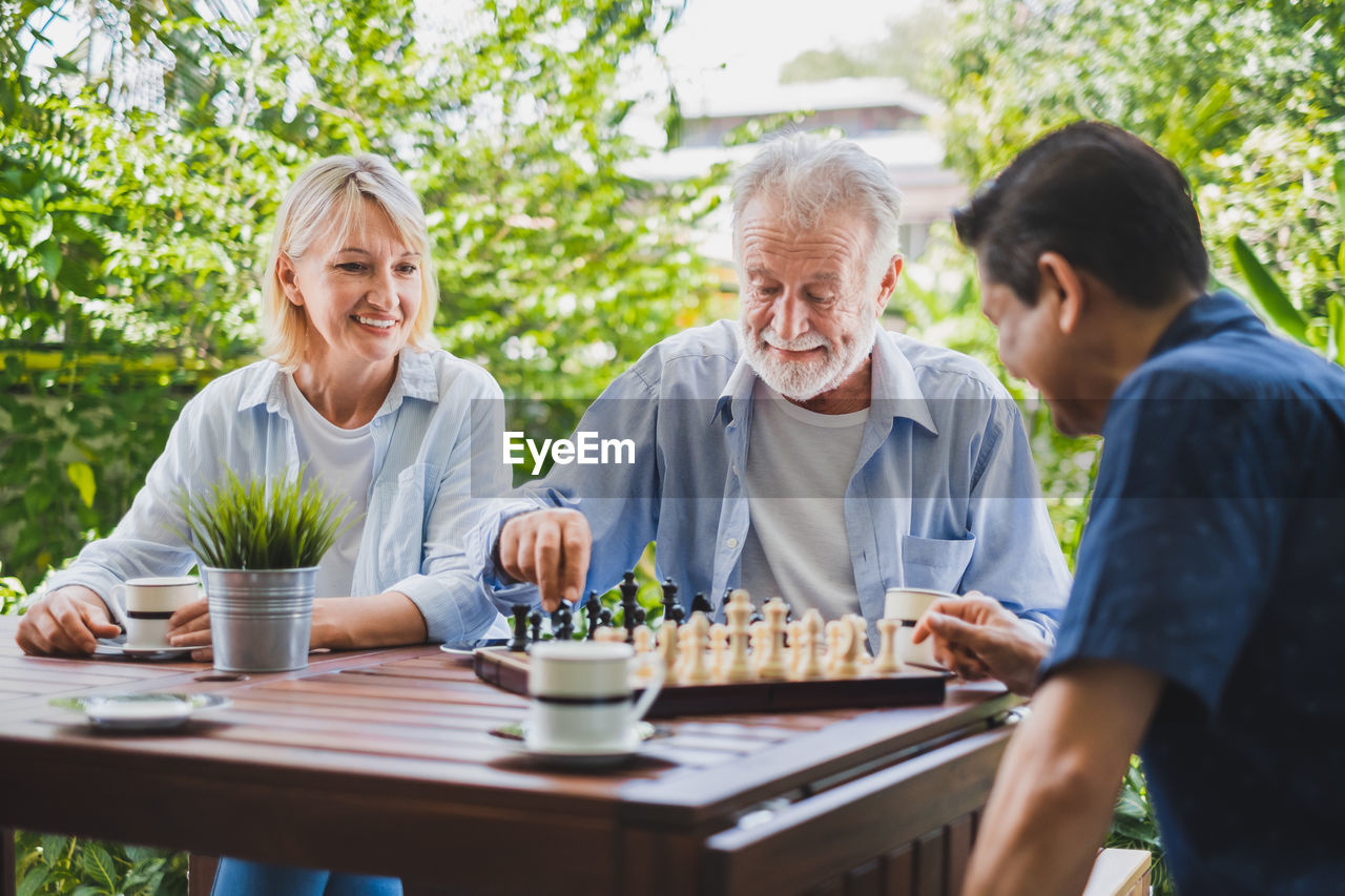 Smiling woman looking at friends playing chess on table