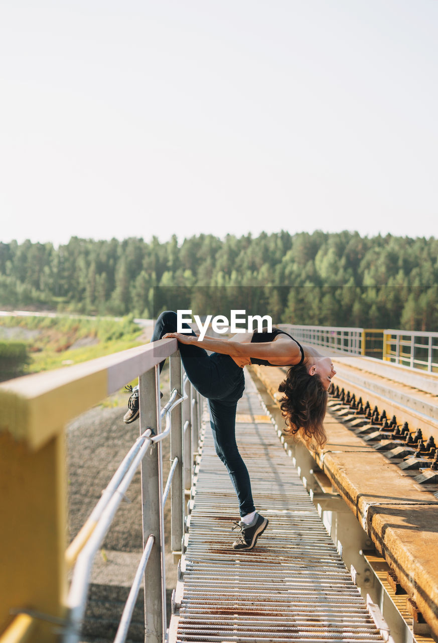 Full length of woman exercising on railway bridge against sky