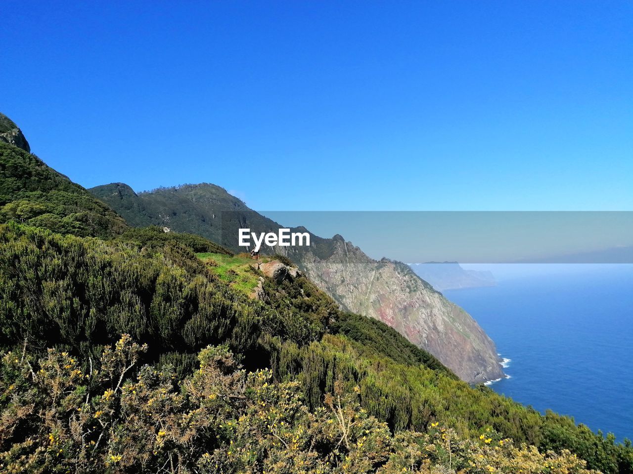 SCENIC VIEW OF SEA BY MOUNTAINS AGAINST CLEAR BLUE SKY