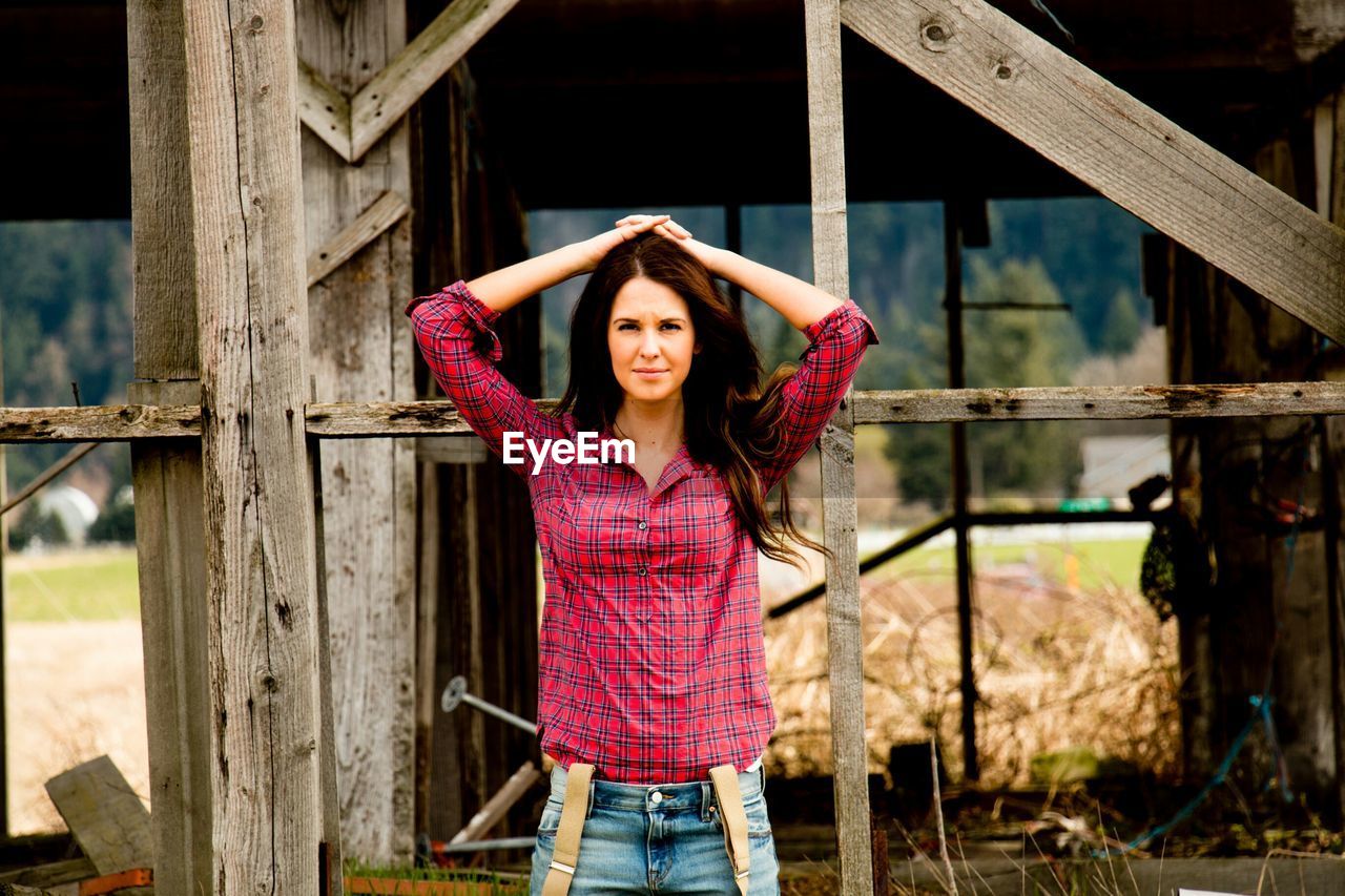 Portrait of beautiful young woman standing against abandoned house