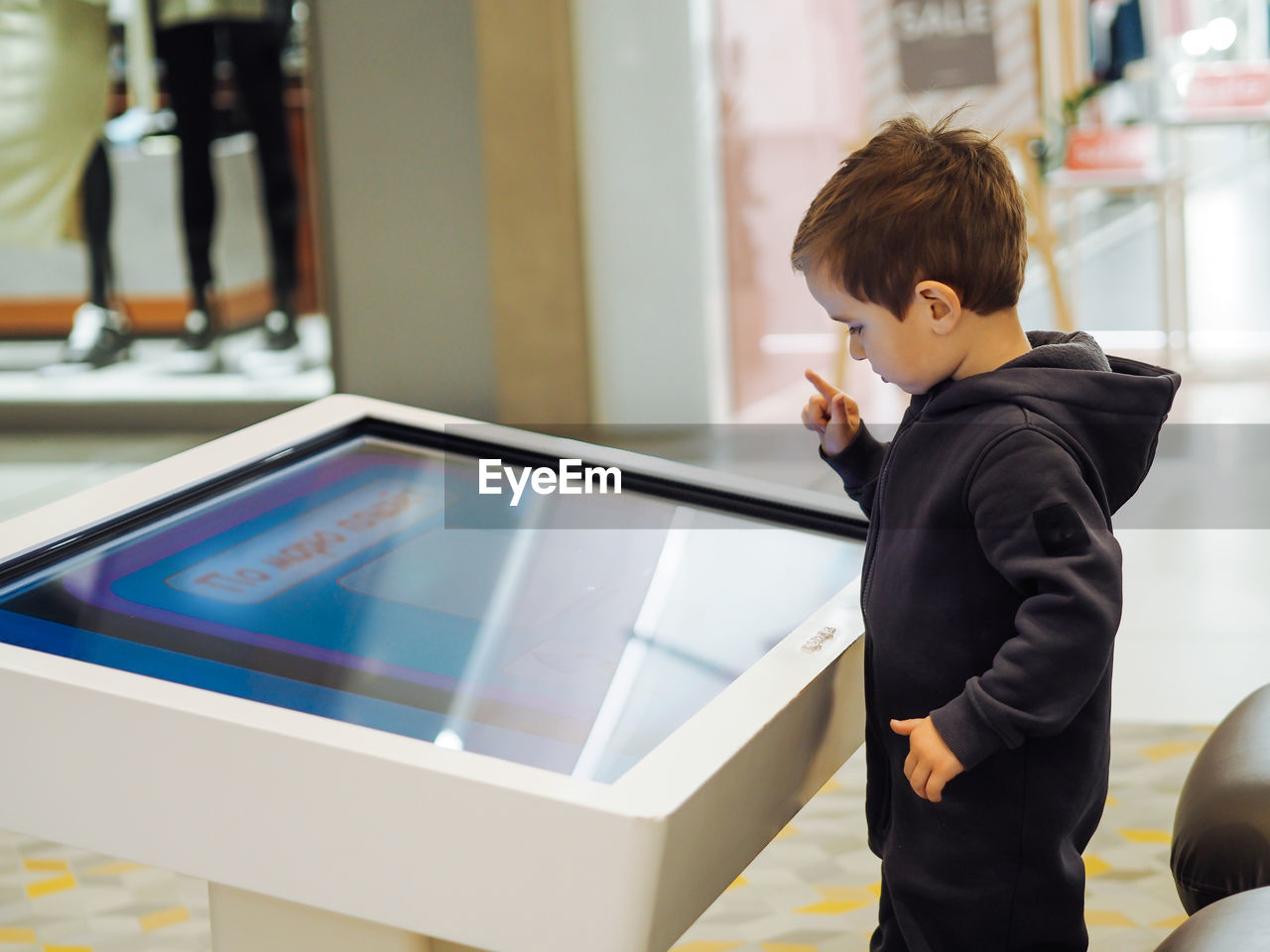 Cute toddler boy using big play tablet in mall