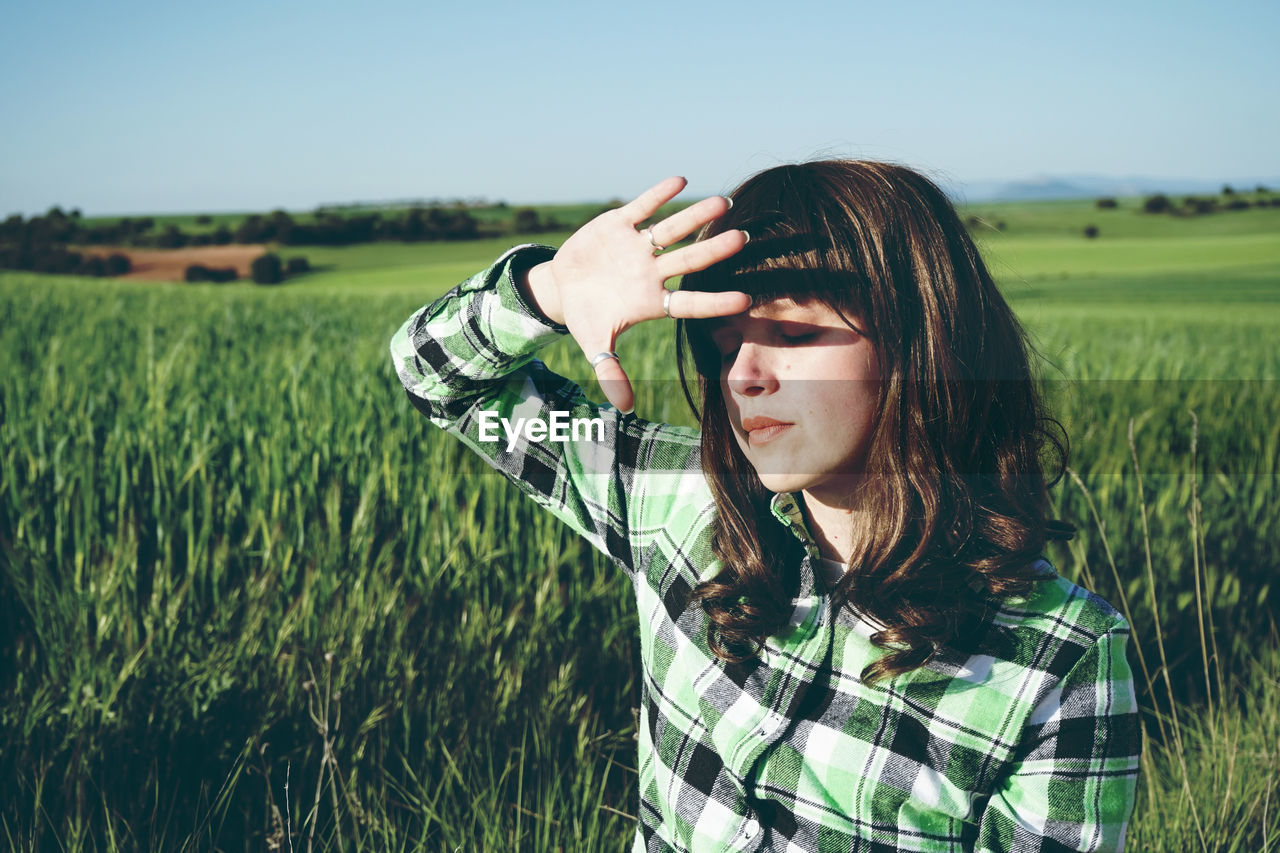 Woman with eyes closed standing on field during sunny day