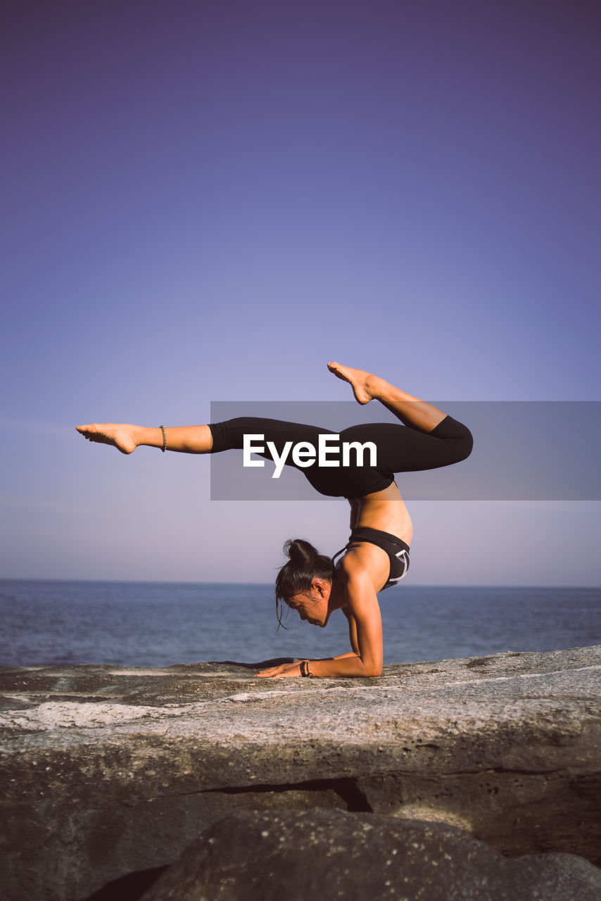 Woman practicing yoga at beach against sky