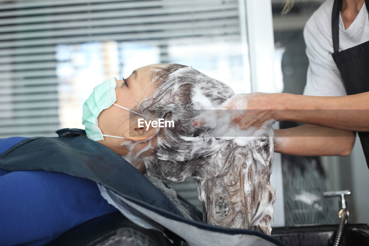 Midsection of hairdresser washing woman hair in salon