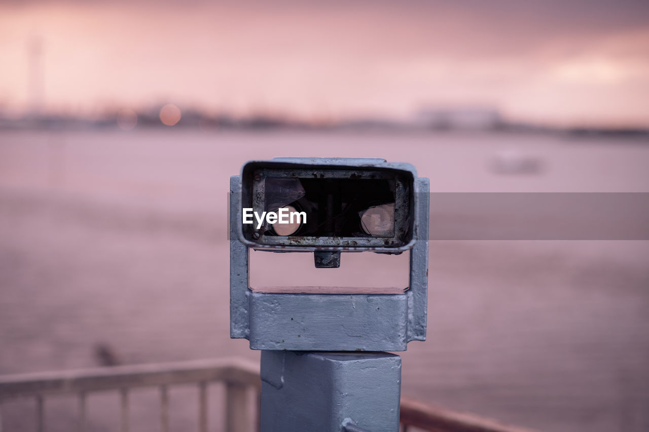 Close-up of coin-operated binoculars by sea during sunset