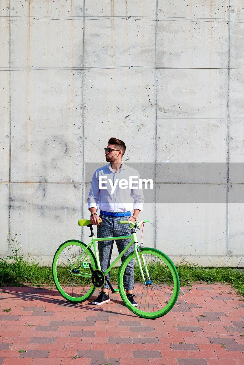 Young bearded man with sunglasses standing with bike outdoors