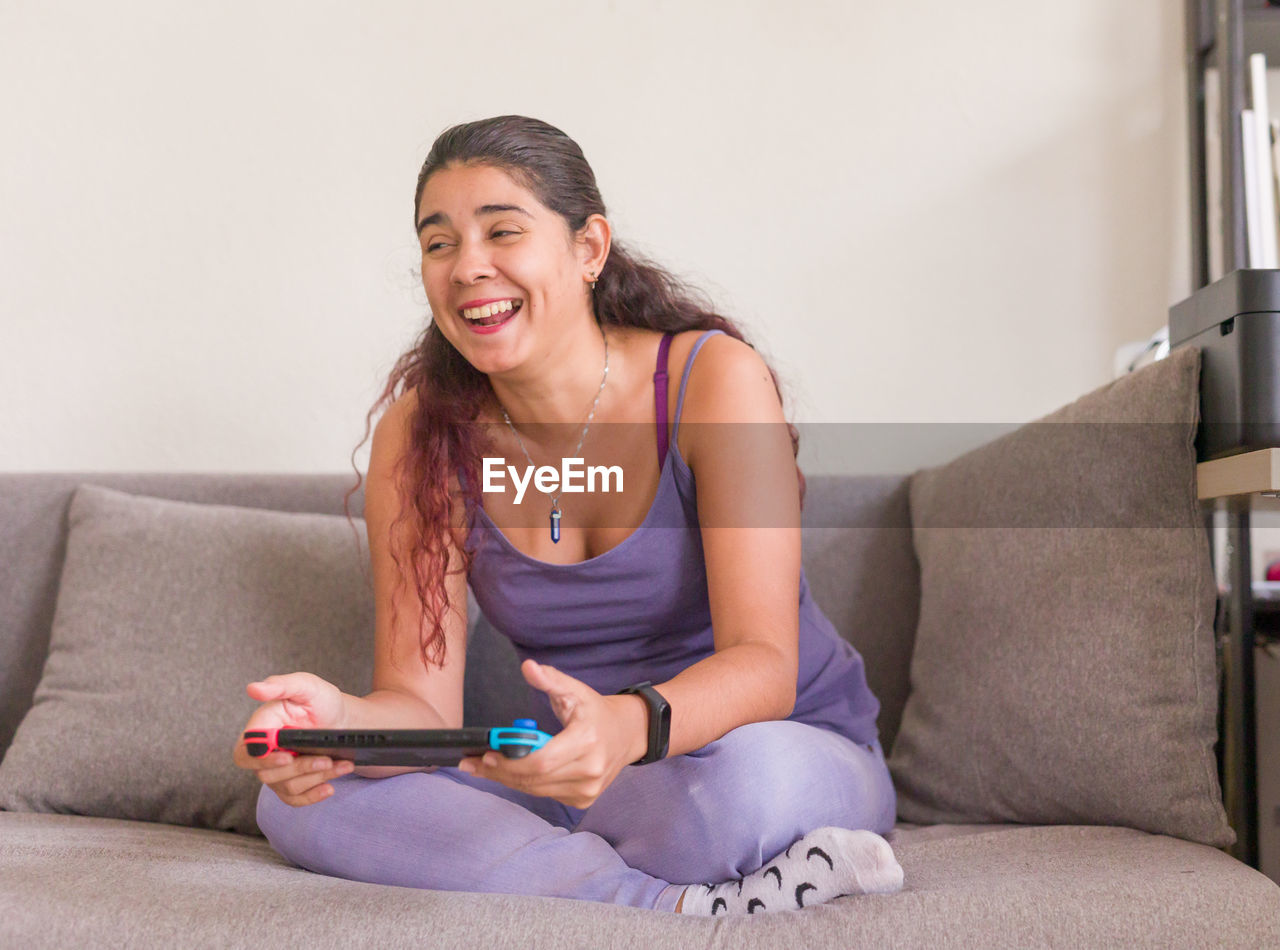 portrait of young woman using mobile phone while sitting on sofa at home