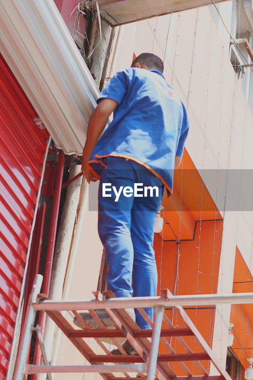 Rear view of man working on a ladder performing paint job