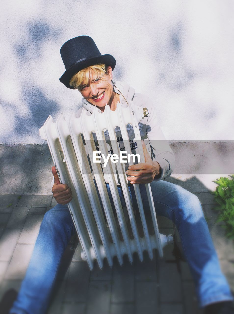 High angle portrait of woman holding radiator while sitting on footpath