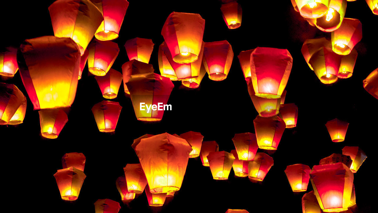 LOW ANGLE VIEW OF ILLUMINATED LANTERNS HANGING AGAINST DARK