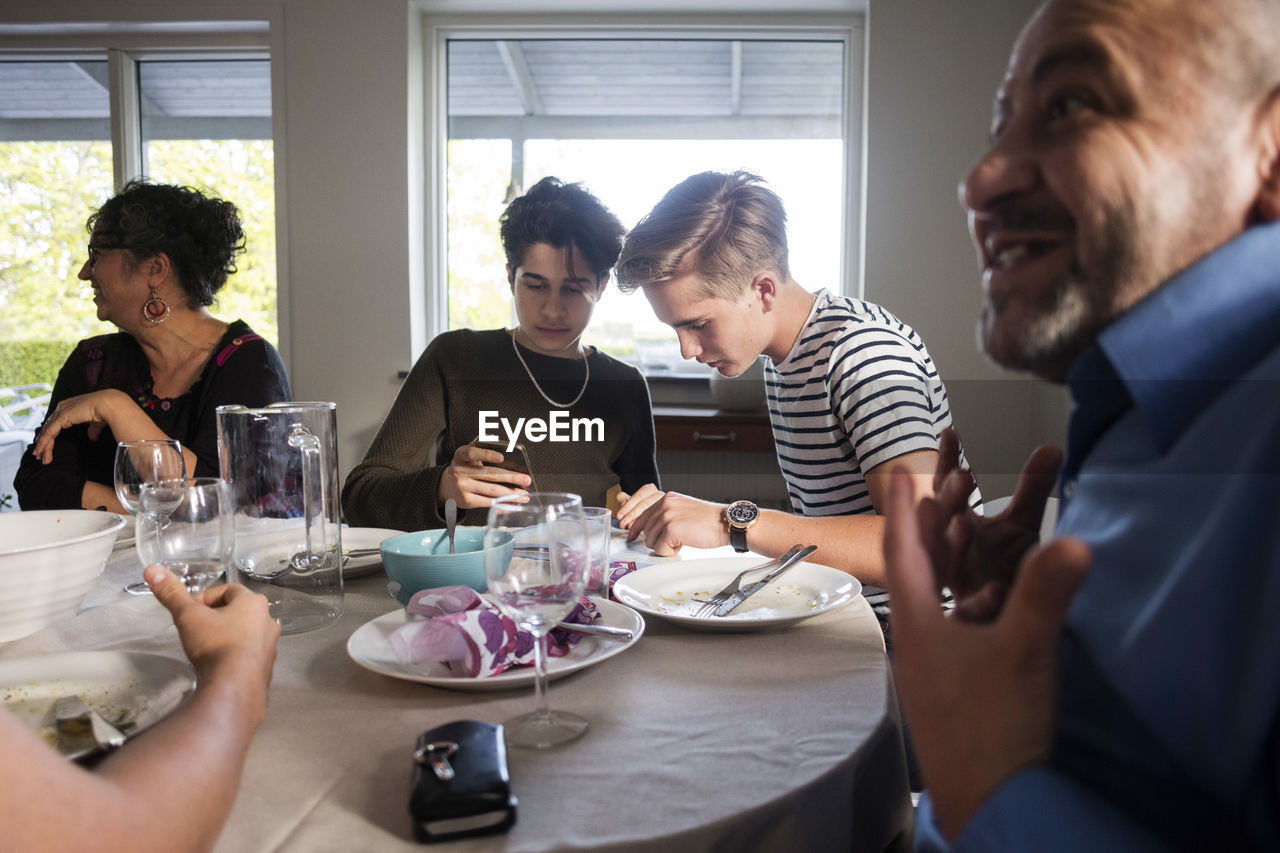 Friends using phone while family talking at dining table in dinner party