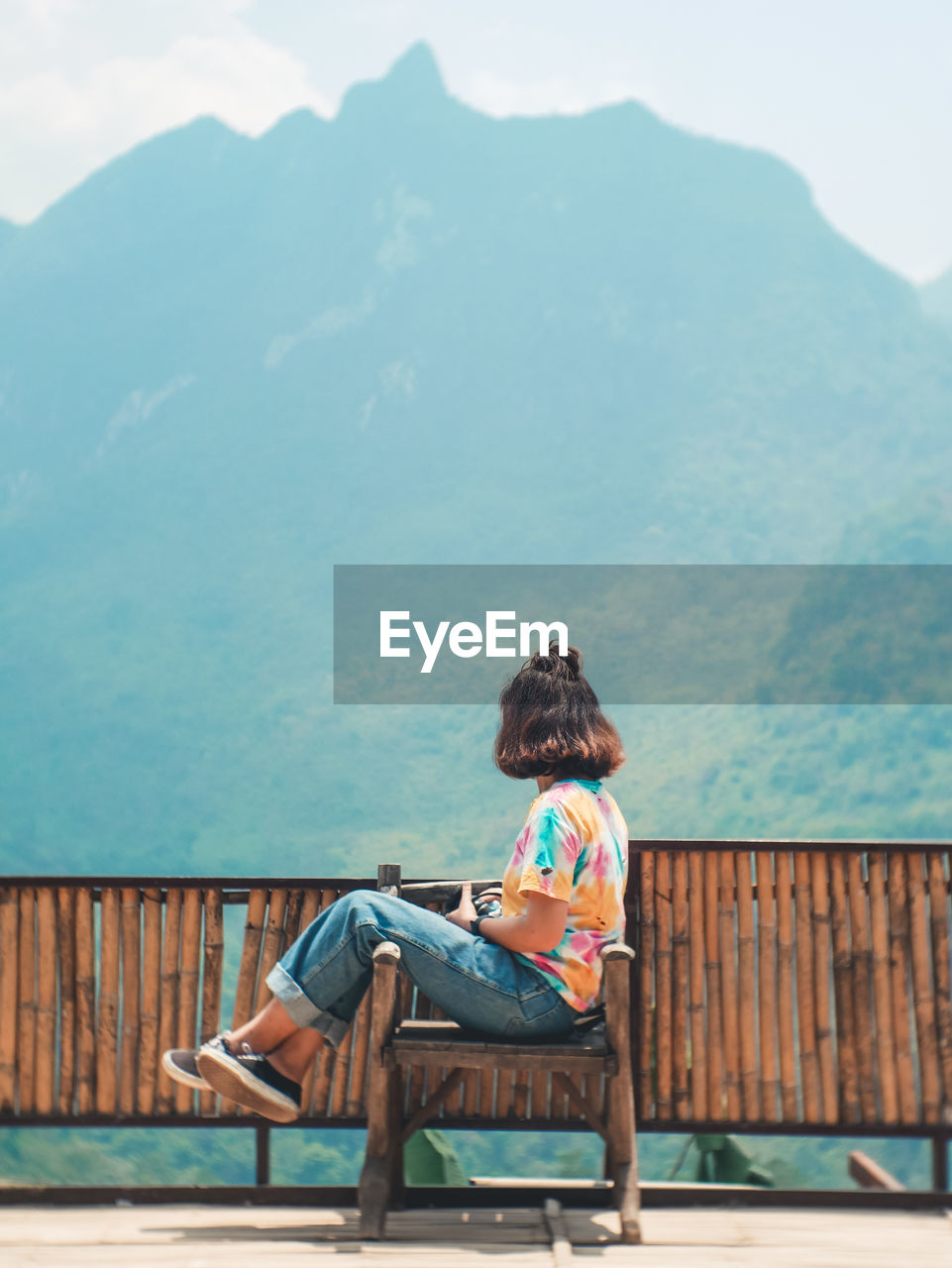 Rear view of woman sitting on bench against mountain