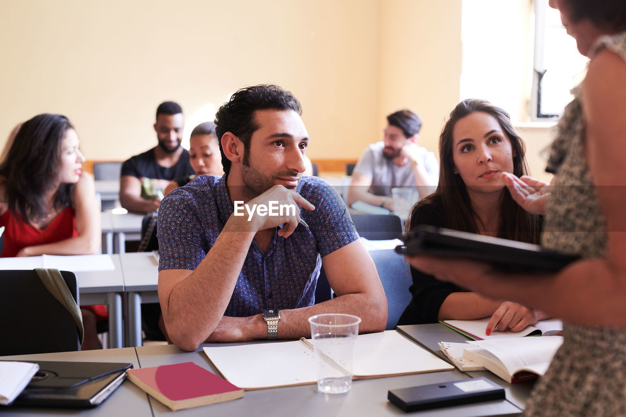 Male and female students looking at teacher explaining in classroom