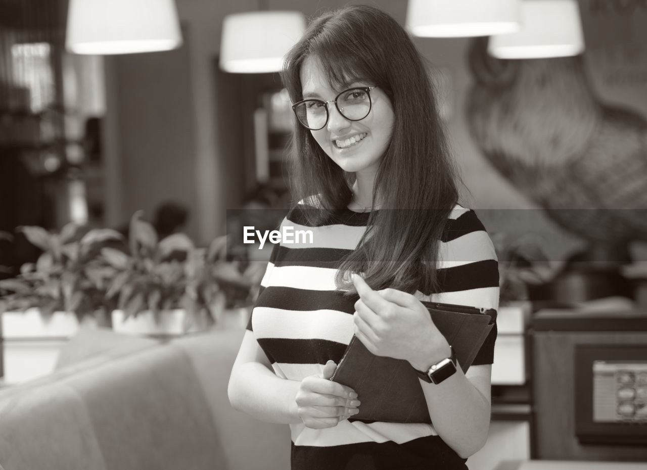 Portrait of confident young woman with digital tablet standing in restaurant