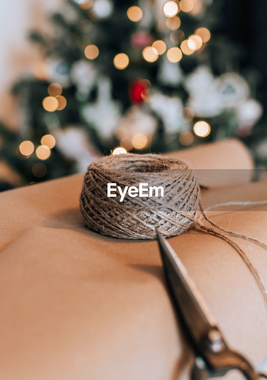 Close-up photo of wrapping paper, twine and scissors in front of christmas tree