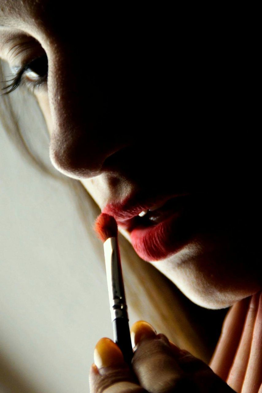 Cropped image of woman applying red lipstick with brush