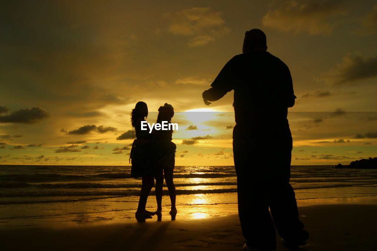 Silhouette family standing at beach against orange sky