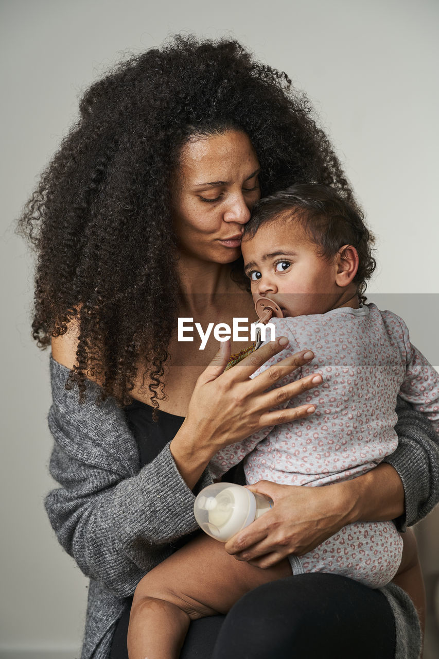 Curly haired woman carrying daughter on gray background