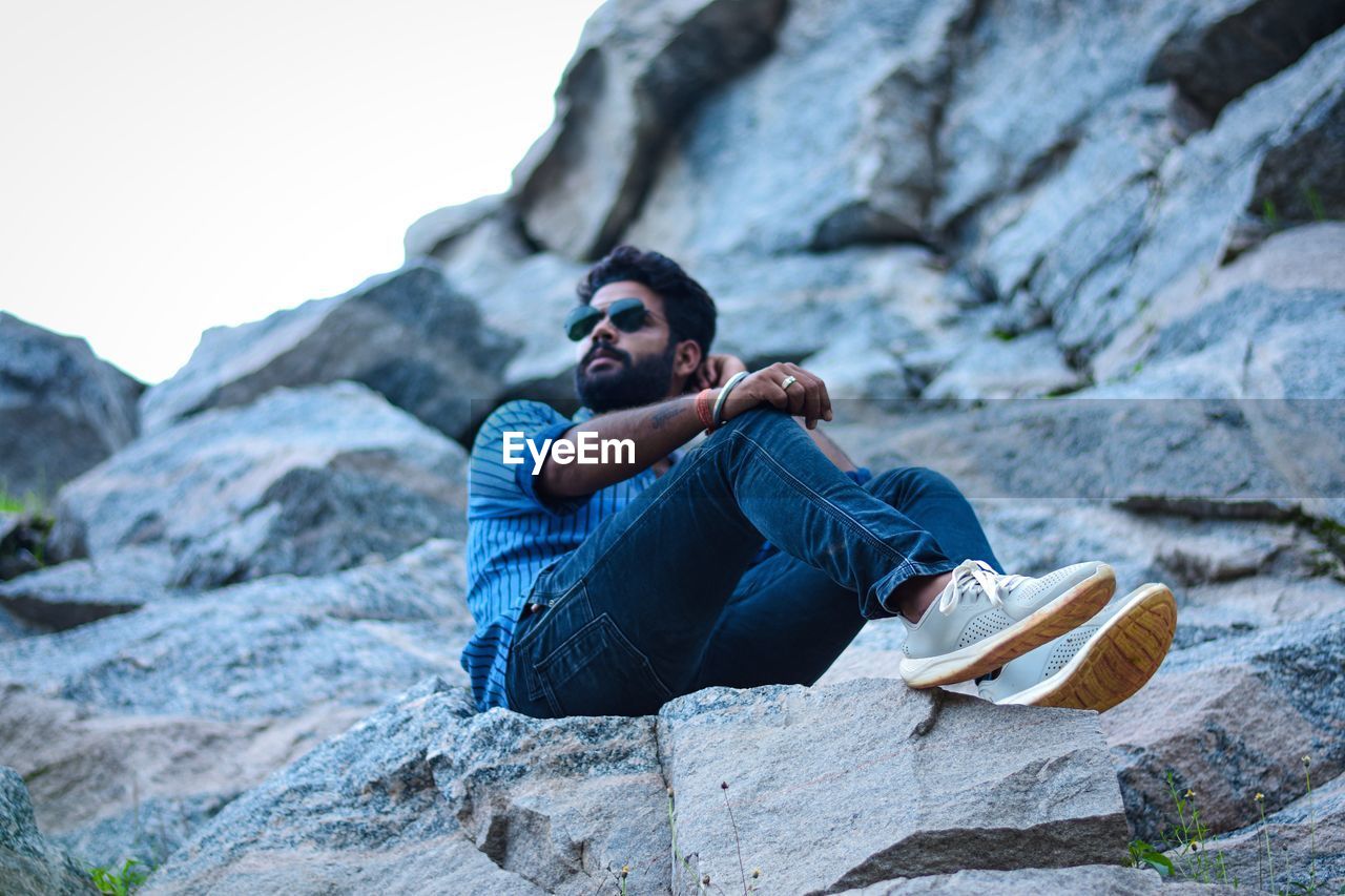 Young bearded man sitting on rock and posing