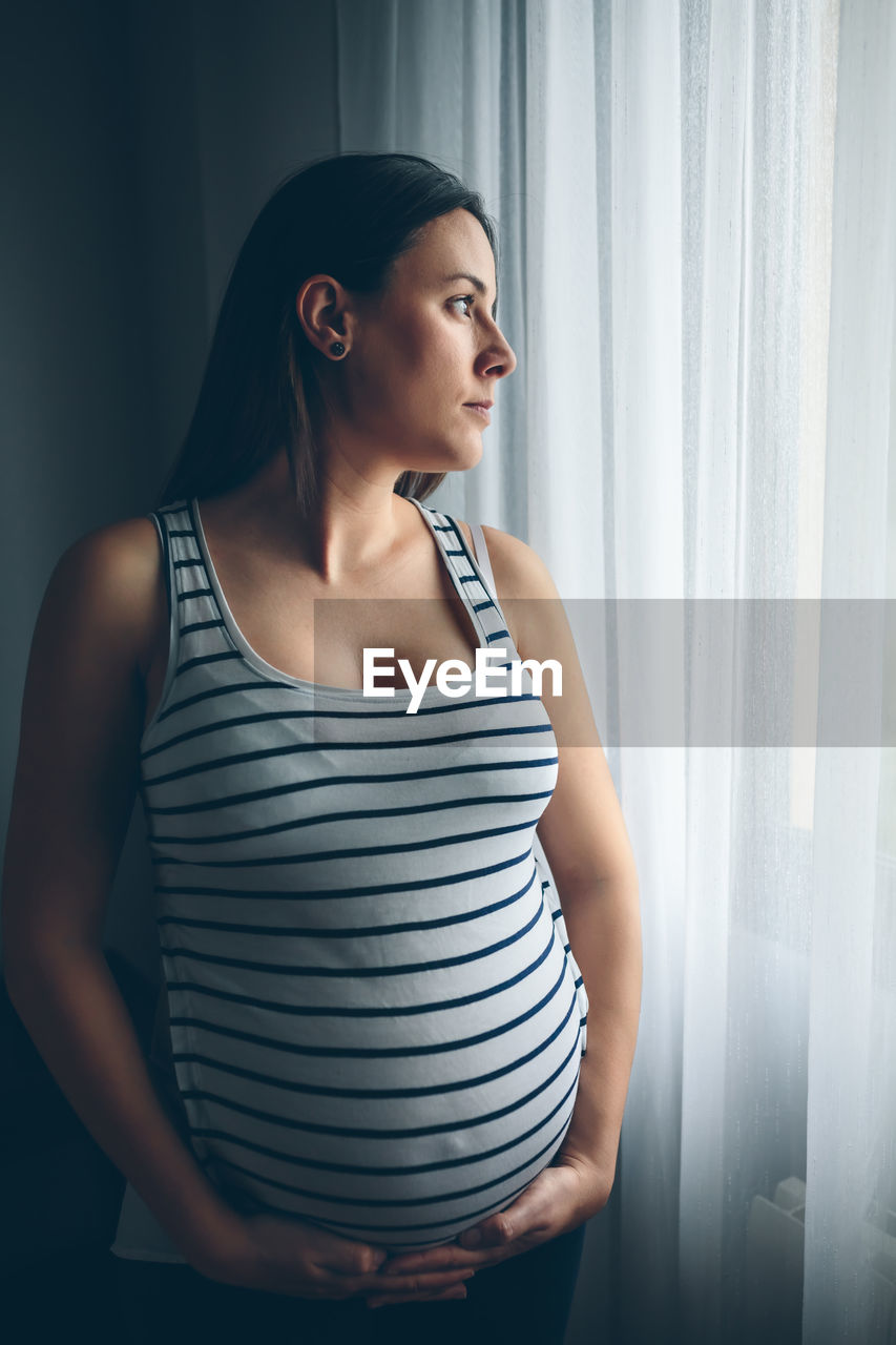 Pregnant woman standing by window at home