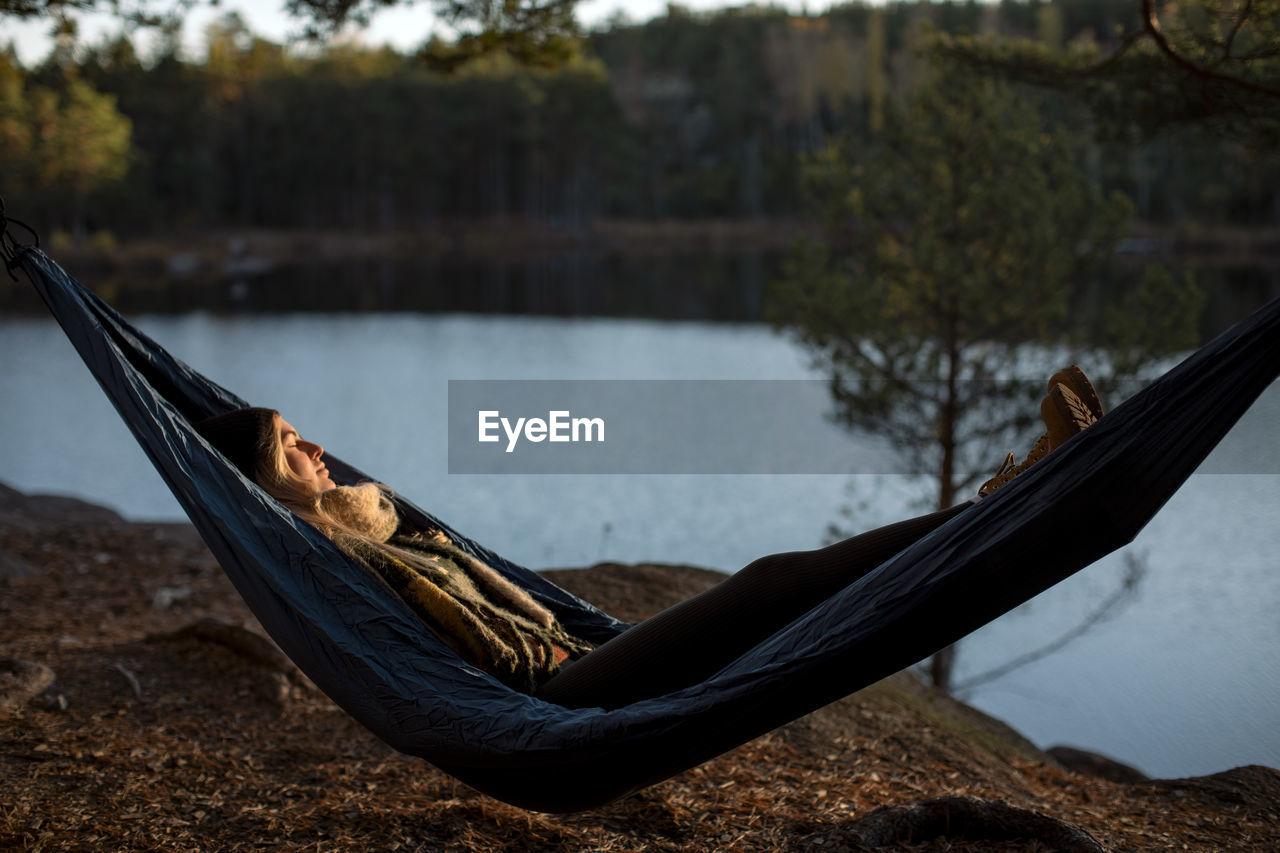 Young woman sleeping on hammock at lakeshore during sunset