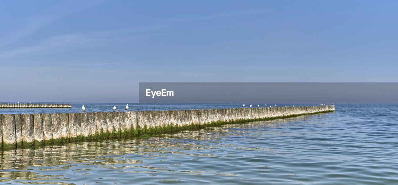 WOODEN POSTS ON SEA AGAINST SKY