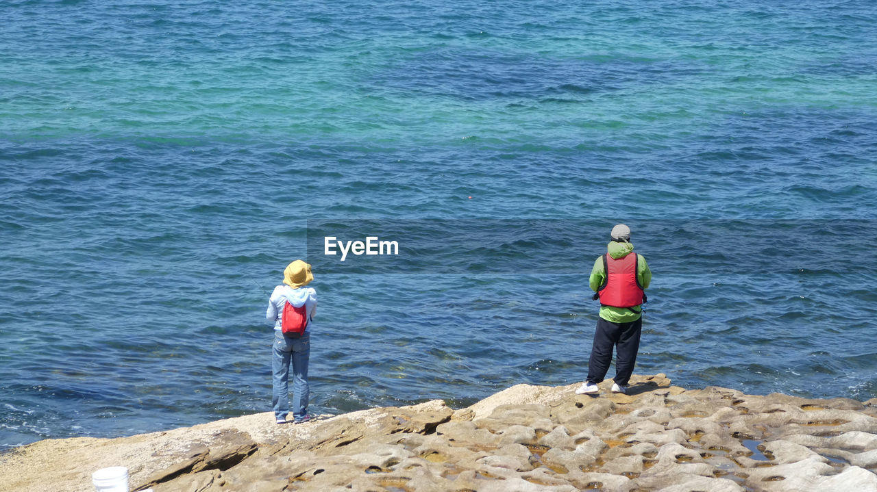 REAR VIEW OF FRIENDS STANDING ON SHORE