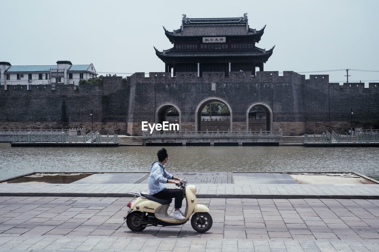 FULL LENGTH OF MAN RIDING MOTORCYCLE IN FRONT OF BUILDING