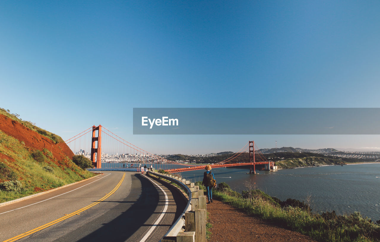 Mid adult woman walking at roadside against golden gate bridge